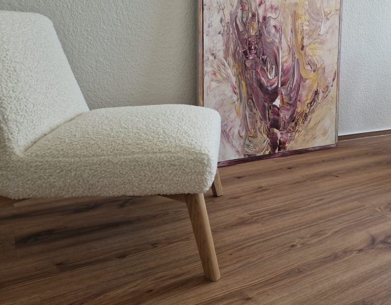 Beige Sessel mit Holzbeinen vor einem bunten, abstrakten Gemälde. Holzfußboden.