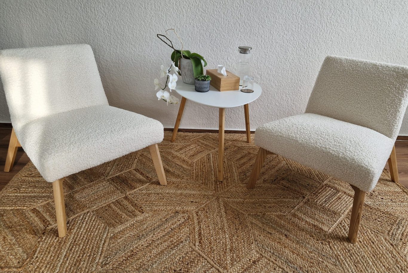 Zwei weiße Stühle mit Holzbeinen neben einem kleinen Tisch auf einem Teppich.