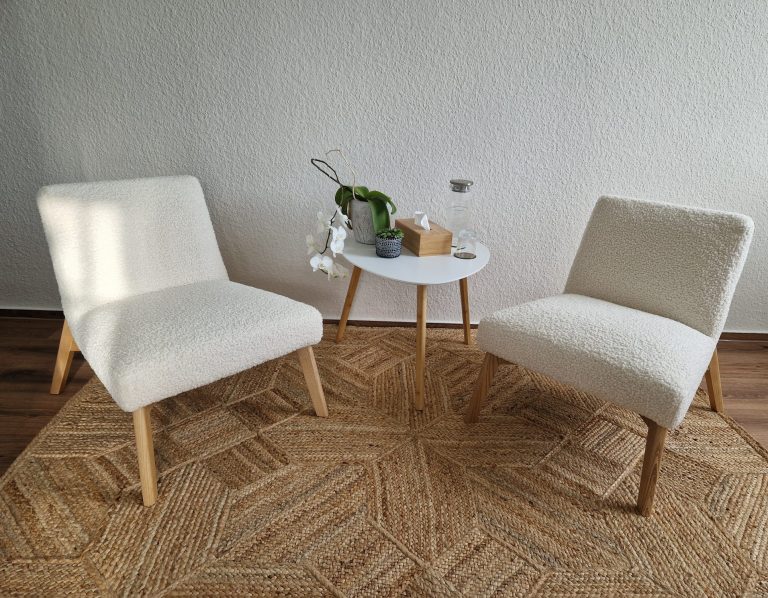 Zwei bequeme, weiße Stühle stehen neben einem kleinen Tisch auf einem Teppich.